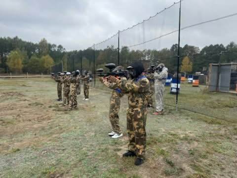 Uczestnicy w maskach ochronnych i strojach maskujących podczas gry w paintball.