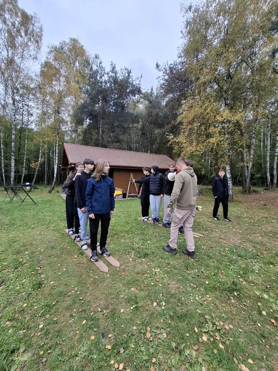 Uczniowie wspólnie pokonują trasę na wieloosobowych drewnianych nartach.