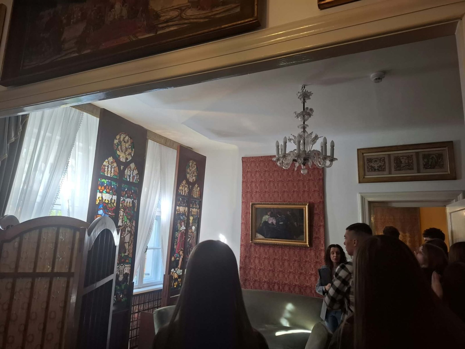 Przewodniczka opowiada uczniom w pokoju z witrażami.