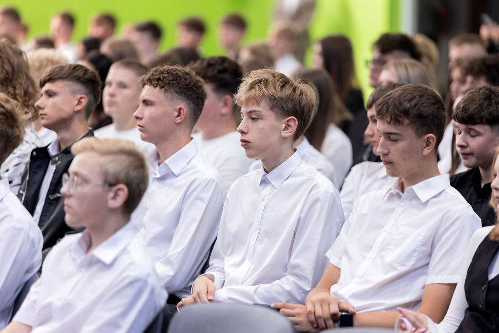 Pierwszoklasiści słuchają wystąpień podczas rozpoczęcia roku szkolnego.