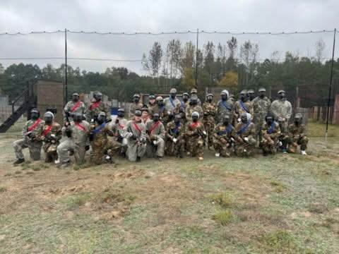 Wspólne zdjęcie uczestników paintballu w strojach maskujących i maskach ochronnych.