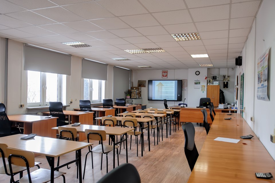 Pracownia z ławkami, zestawami słuchawkowymi i ekranem przy tablicy.