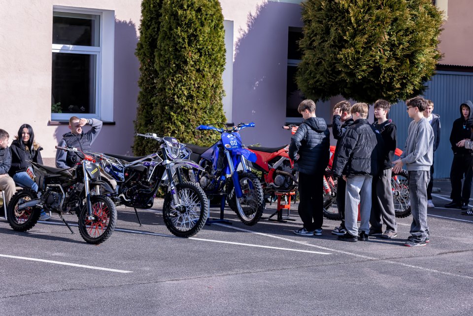 Odwiedzający oglądają motocykle ustawione przed szkołą.