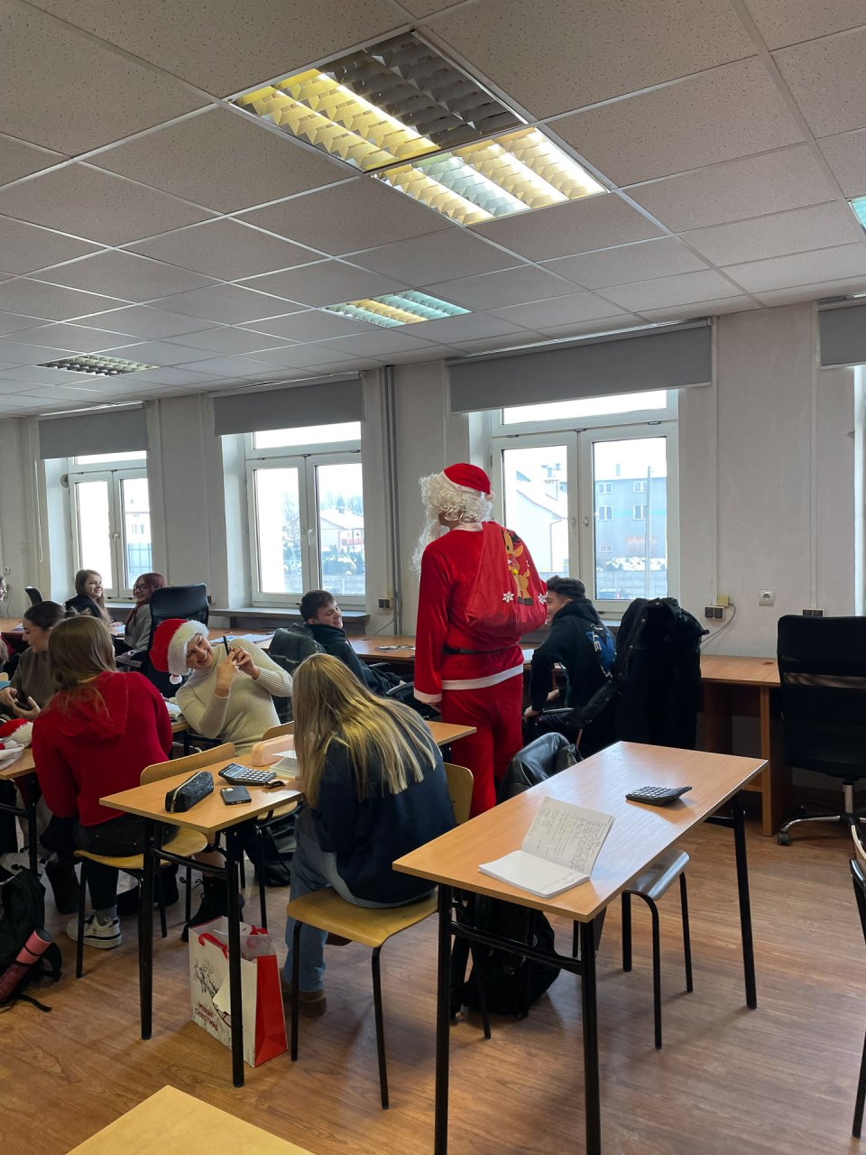 Świąteczne odwiedziny Mikołaja wśród uczniów siedzących przy stolikach.