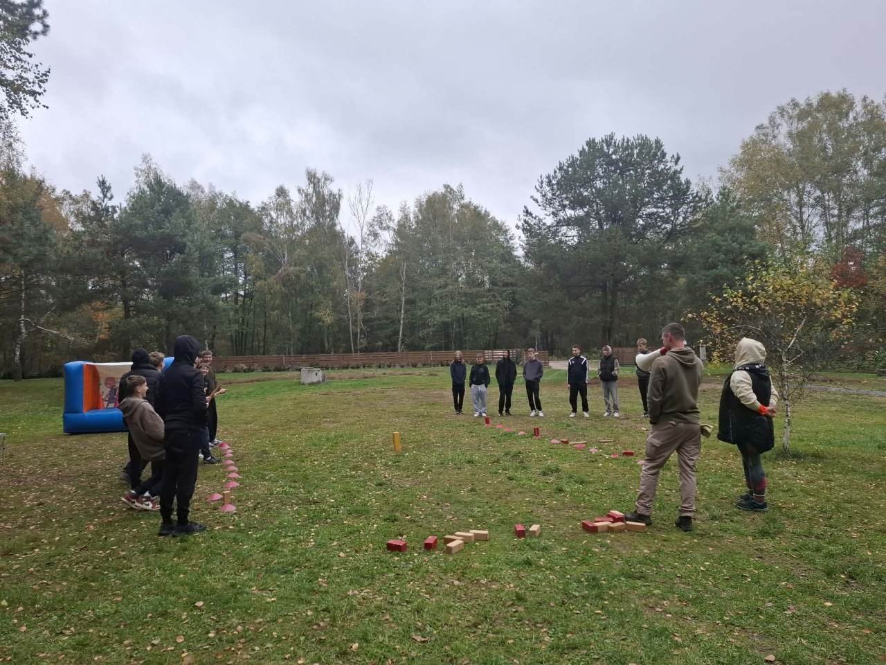 Dwie drużyny uczniów uczestniczą w zabawie zręcznościowej na polanie.