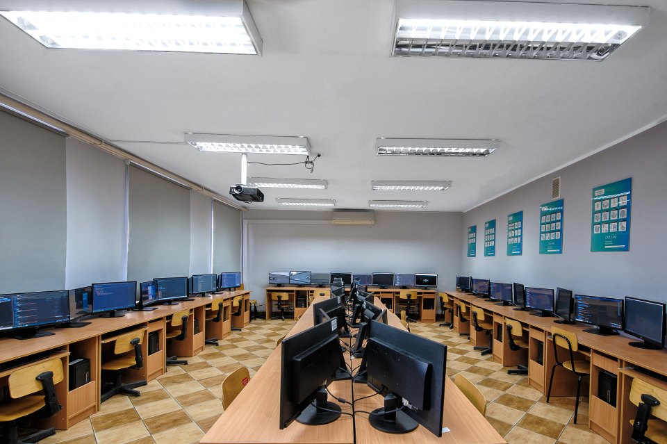 Pracownia komputerowa z monitorami ustawionymi wzdłuż ścian i pośrodku sali.