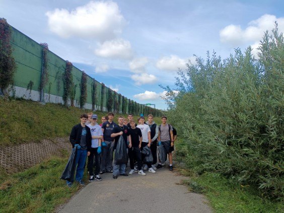Grupa uczniów z workami na odpady stoi na ścieżce.