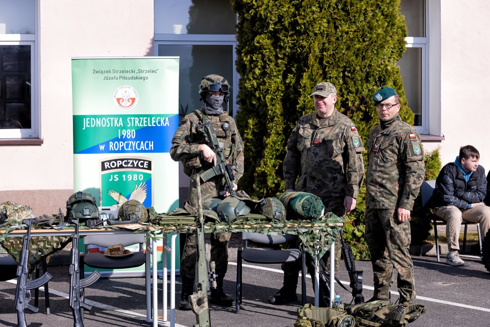 Osoby w mundurach prezentują wyposażenie przy stoisku jednostki strzeleckiej.