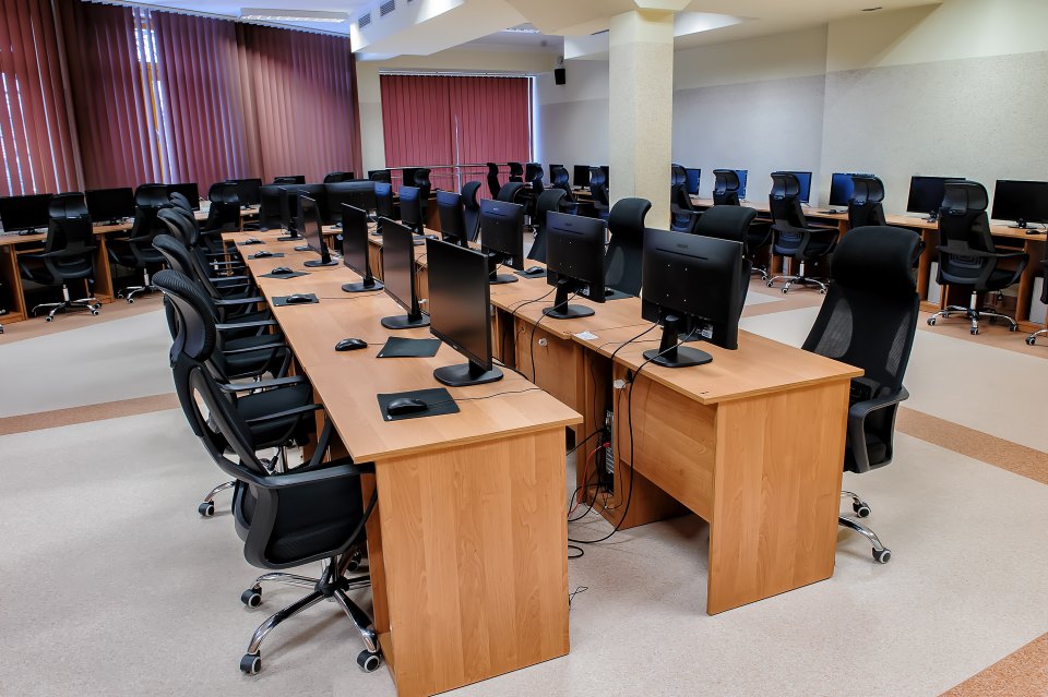 Biurka i zestawy komputerowe w szkolnej pracowni.