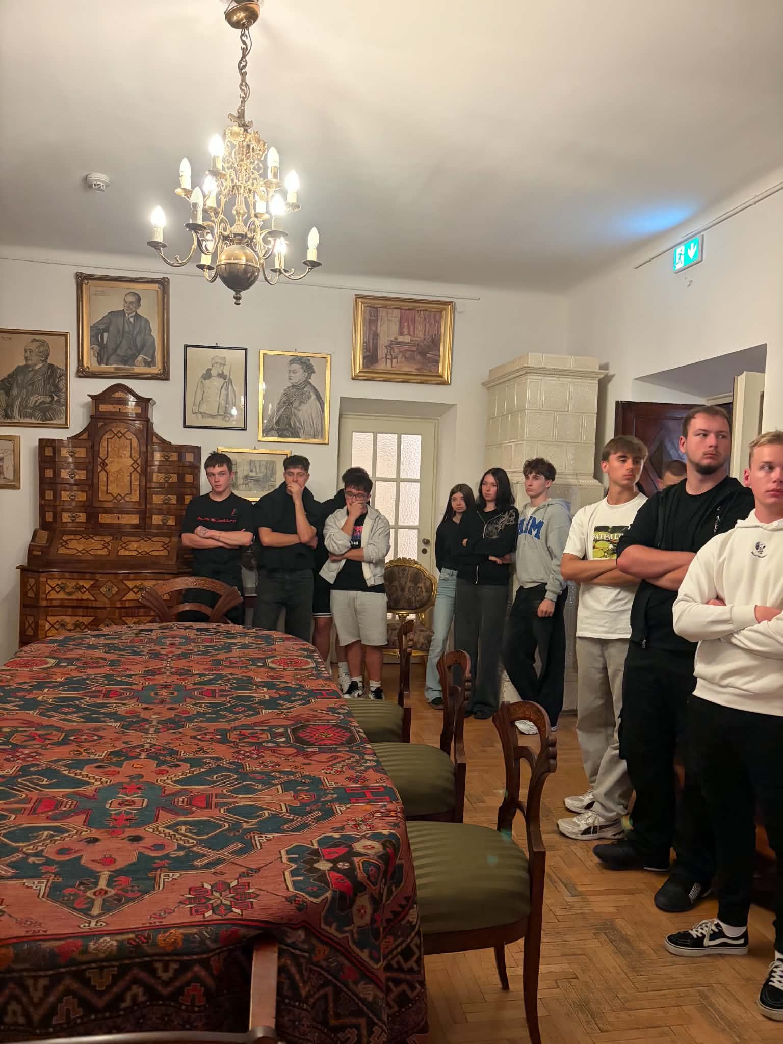 Uczniowie zwiedzają pokój Rydlówki z zabytkowym stołem i portretami.