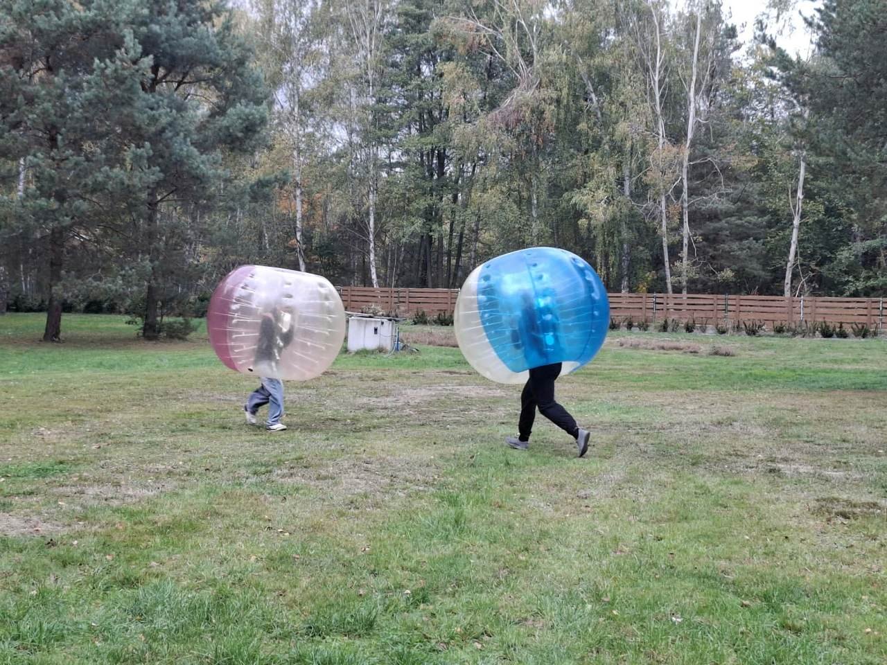 Uczestnicy zabawy poruszają się po trawie w dużych dmuchanych kulach.