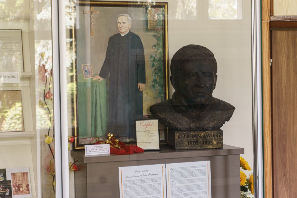 Zbliżenie popiersia patrona i pamiątek w szkolnej gablocie.