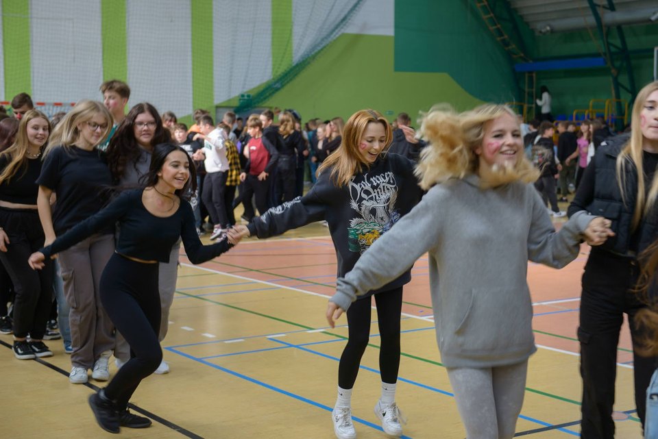 Uczestnicy otrzęsin tańczą wspólnie w hali sportowej.