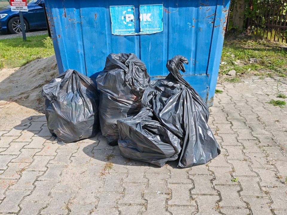 Zebrane worki z odpadami stoją przy kontenerze.