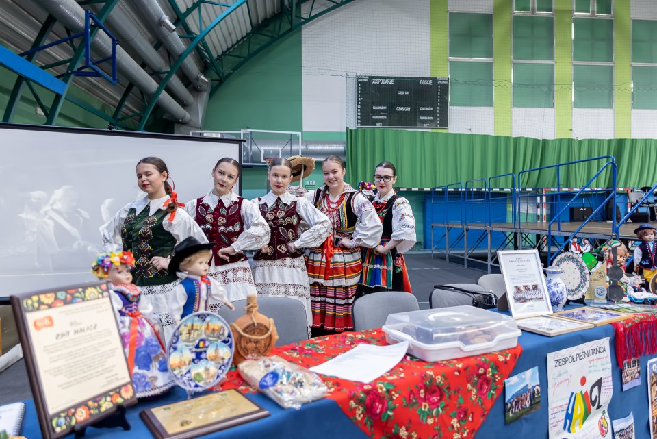 Młodzież w strojach ludowych przy stoisku z rękodziełem.