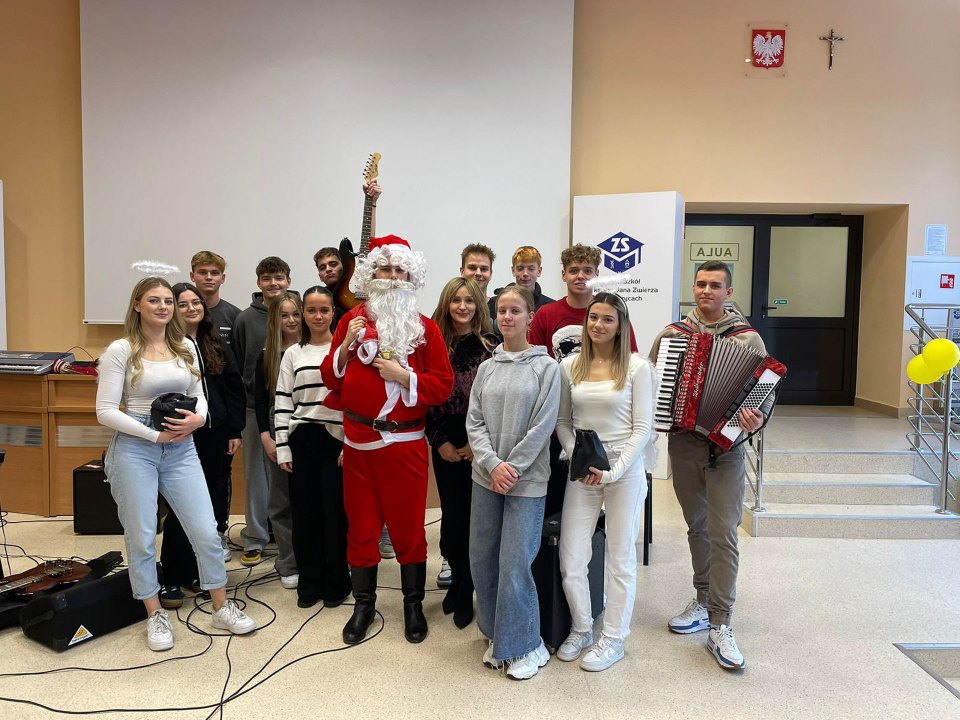 Grupa uczniów z Mikołajem i akordeonistą na szkolnym korytarzu.