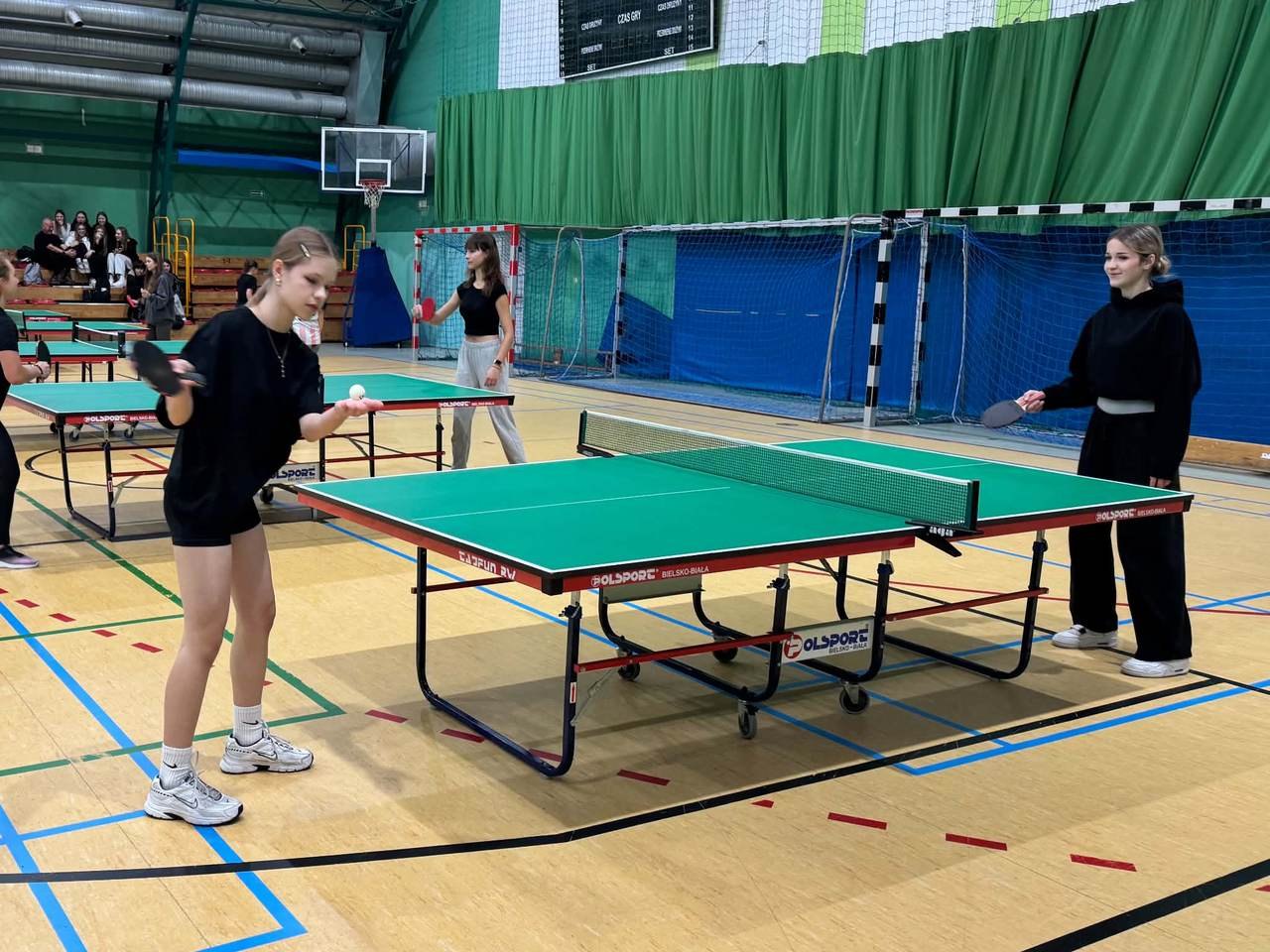 Zawodniczki rozgrywają mecze tenisa stołowego w szkolnej hali sportowej.