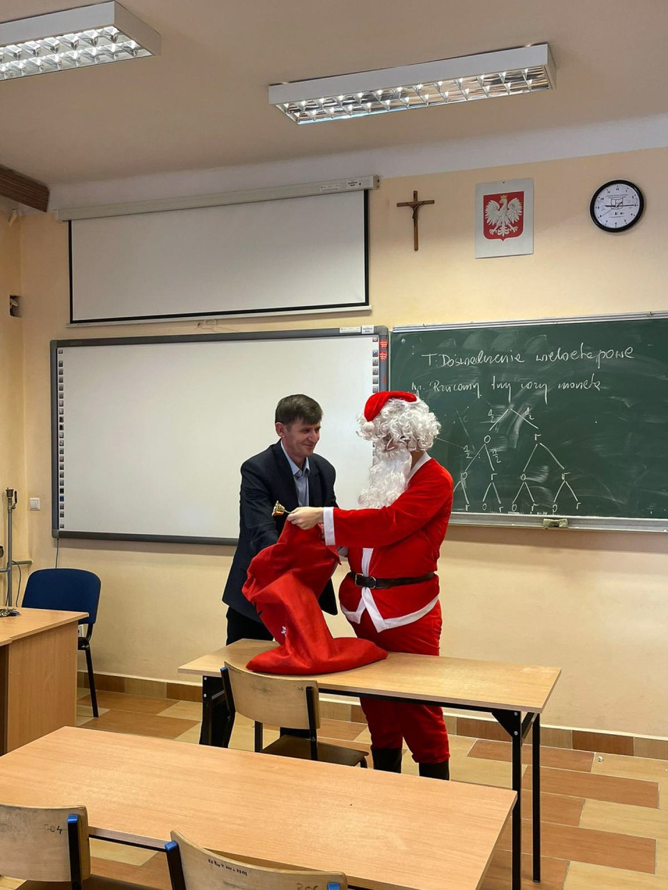 Uczeń odbiera poczęstunek od Mikołaja w sali lekcyjnej.