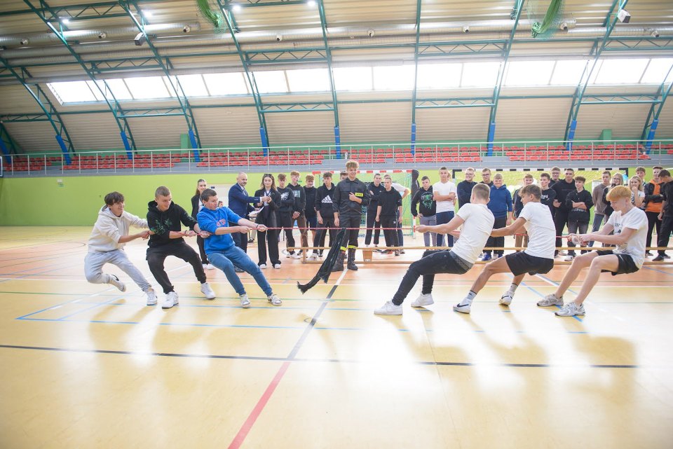 Dwie drużyny przeciągają linę w hali sportowej.