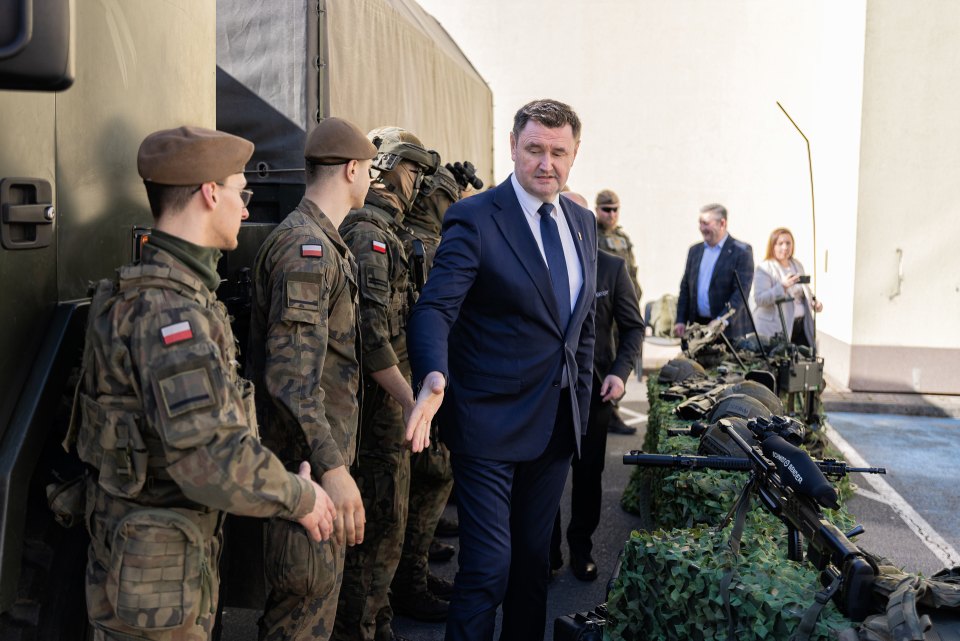 Goście rozmawiają z osobami w mundurach przy wystawie wyposażenia.
