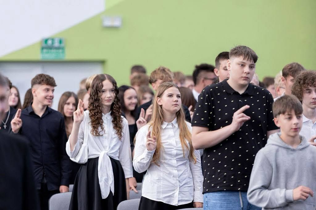 Pierwszoklasiści składają ślubowanie z uniesionymi dłońmi.