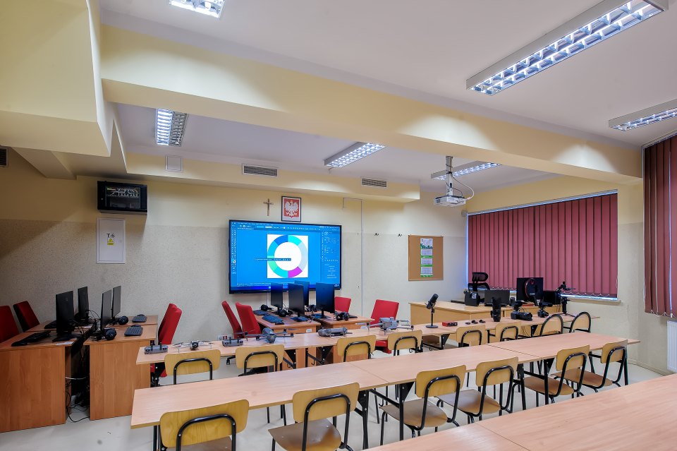 Sala techniczna z komputerami, ekranem i wyposażeniem na ławkach.