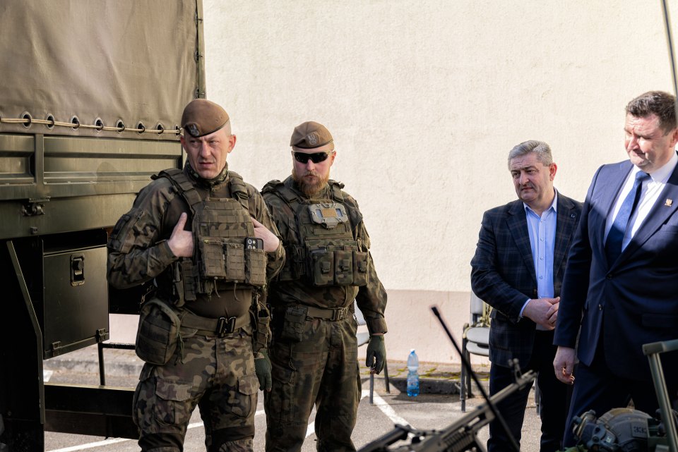 Osoby w mundurach i goście przy stanowisku pokazowym obok pojazdu wojskowego.
