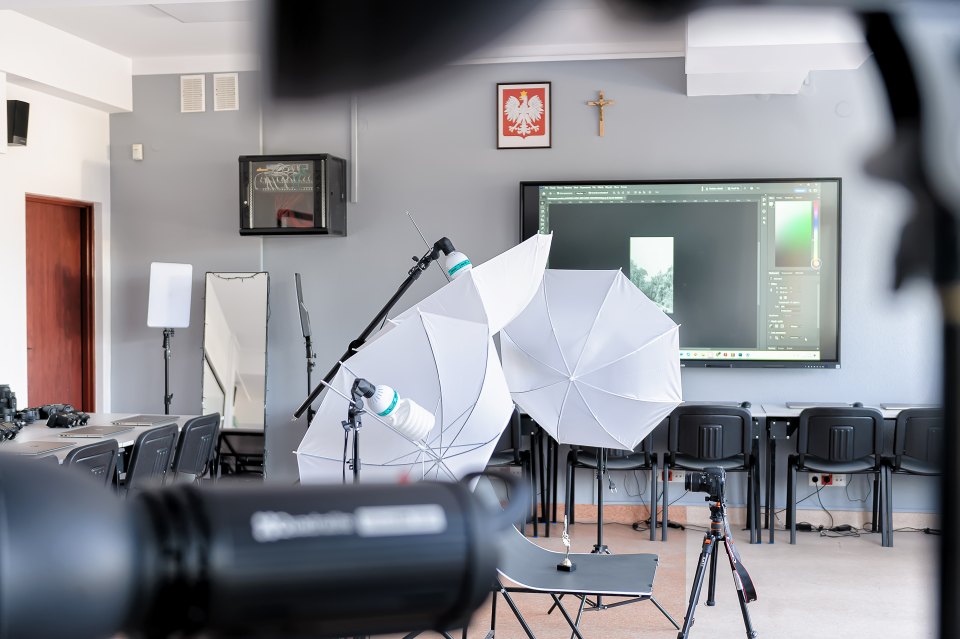Lampa na pierwszym planie i parasole fotograficzne w tle.